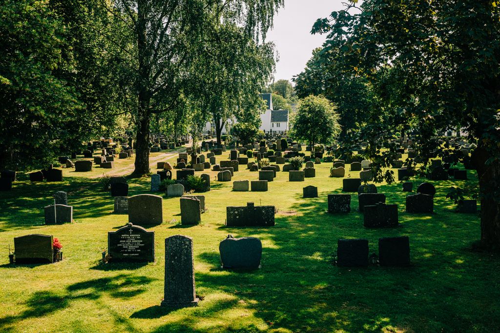 A peaceful cemetery in Norway surrounded by lush green trees under clear daylight.